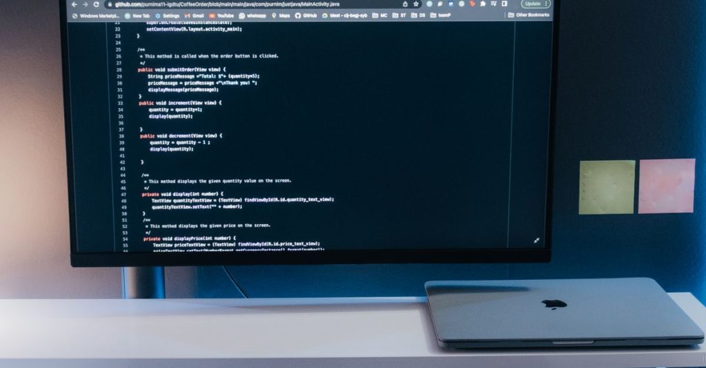 Minimalist home office desk setup with coding on a large monitor, laptop, and gadgets.