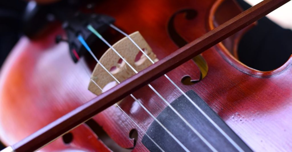 A close-up of a young musician playing a violin outdoors, showing detailed strings and bow.
