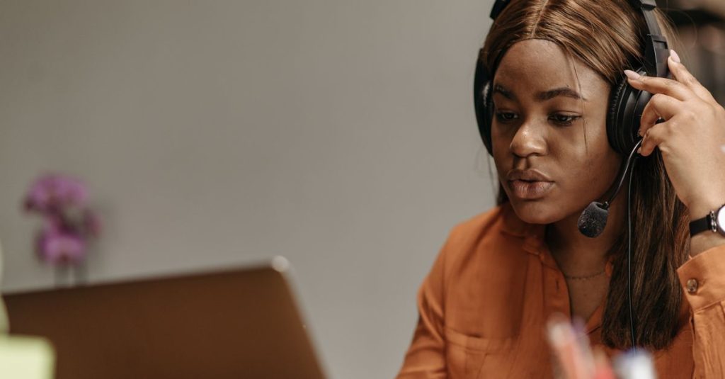 African American woman working in customer support with headphones and laptop indoors.