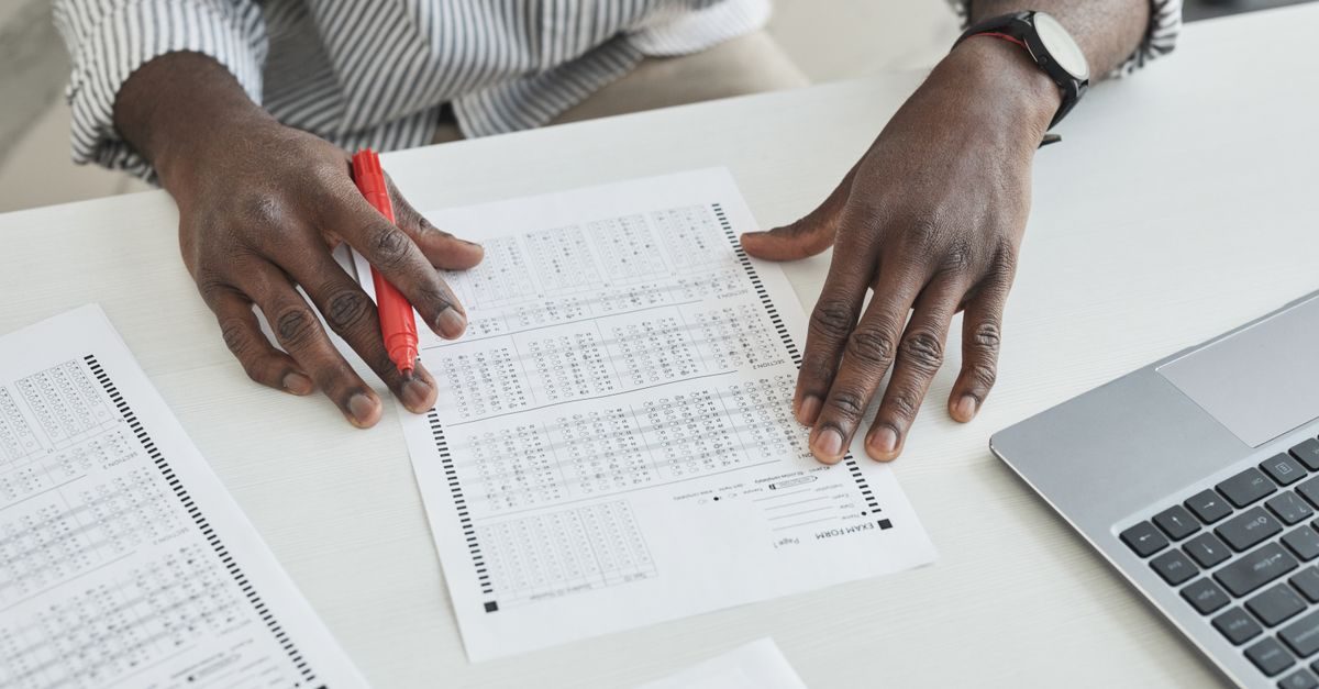 An educator carefully checks exam papers using a red marker at a desk, illustrating focused grading.