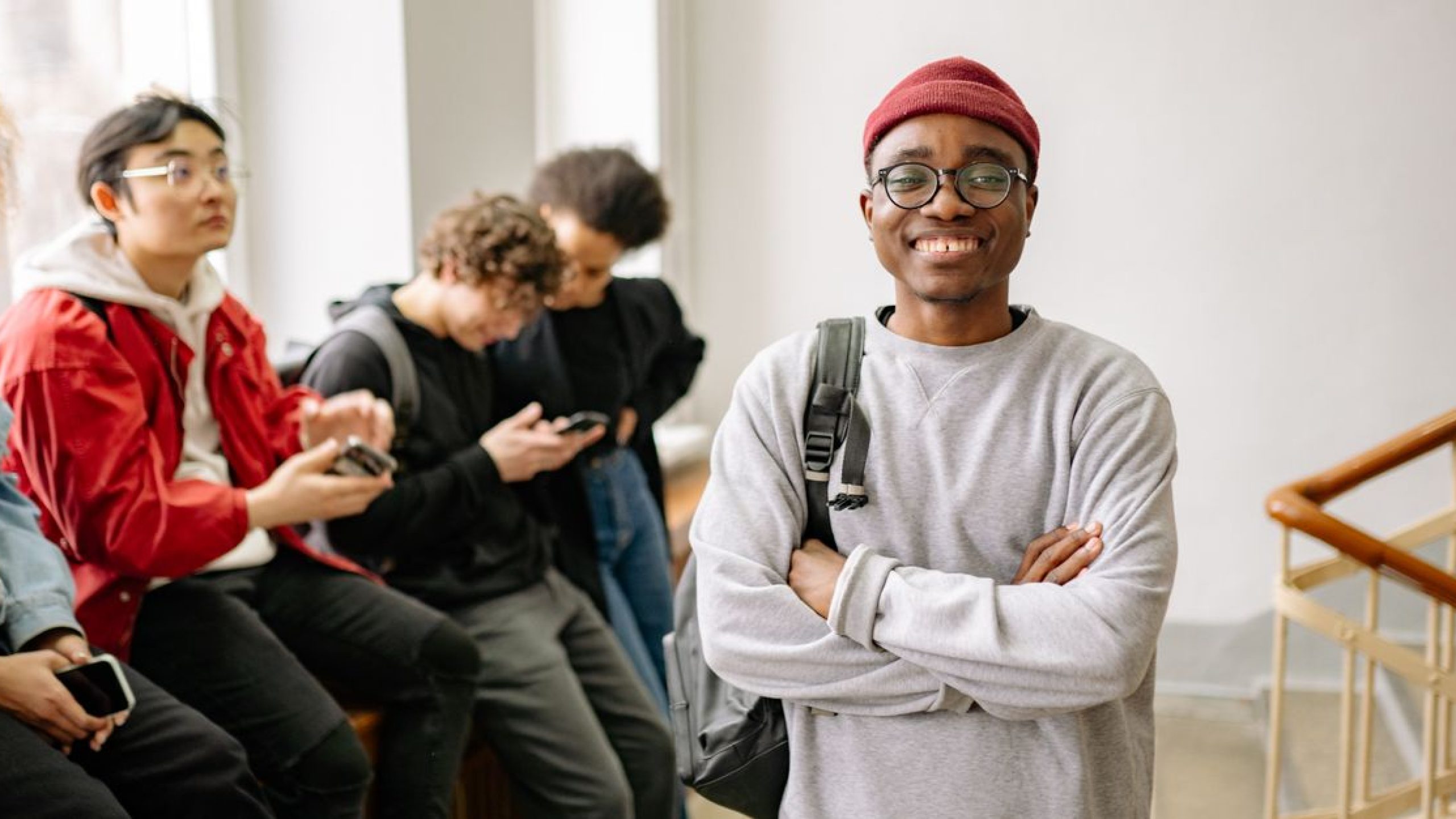 A diverse group of university students indoors, featuring a smiling young man in the foreground.